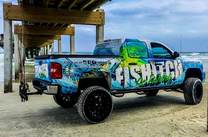 FISHITCH branded fishing truck with custom wrap parked beneath a beach pier